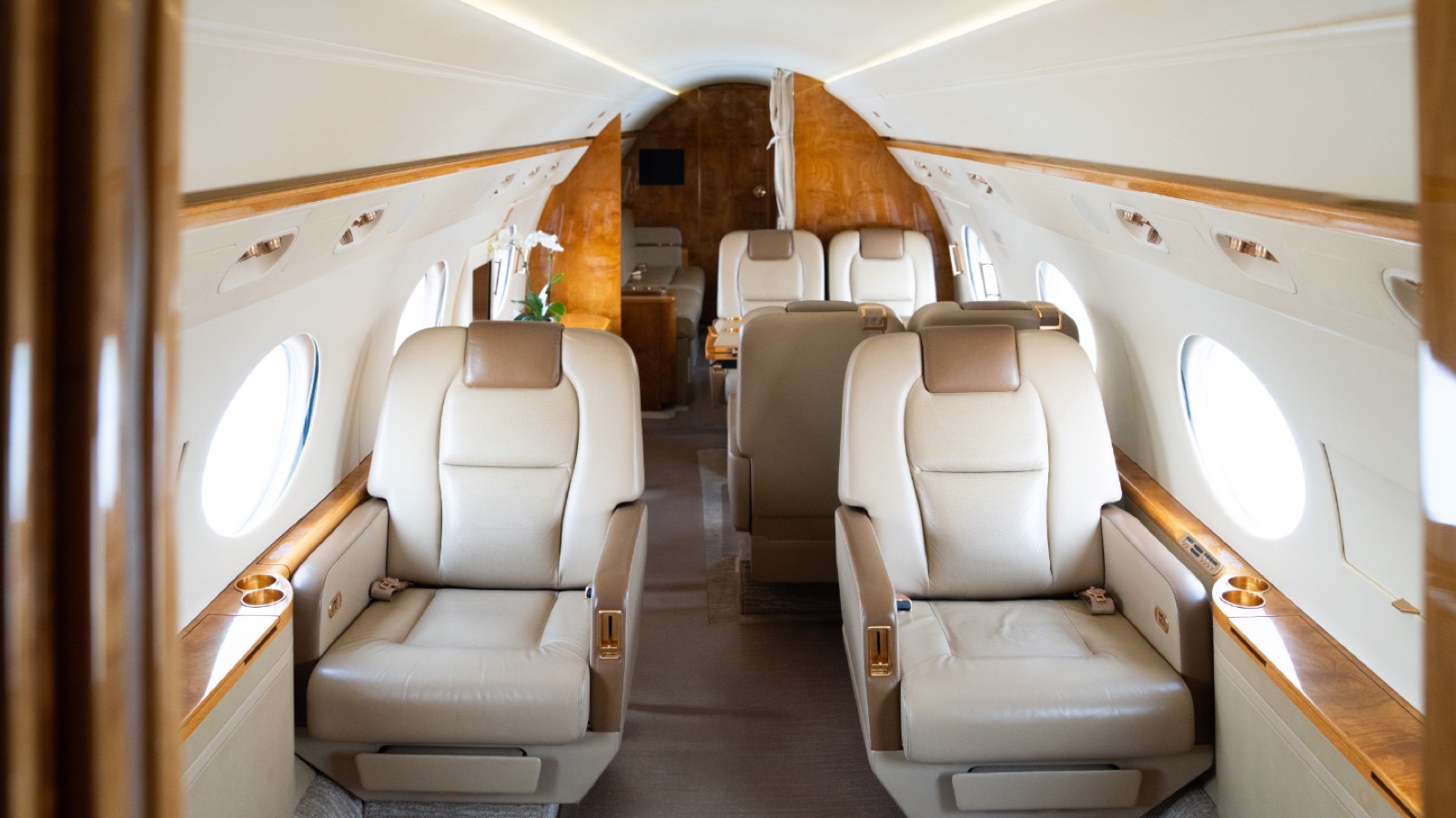 Inside the Gulfstream G450 cabin — ivory leather and honey burl between the signature oval windows